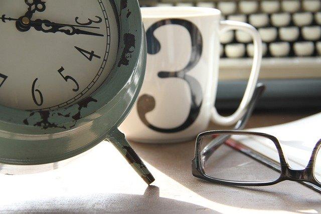 Image d’un environnement de travail contenant une horloge, une paire de lunettes et une tasse.